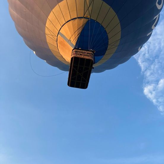 Ein Heißluftballon mit blauem und gelbem Umschlag schwebt am Himmel. Der Korb ist unten befestigt.