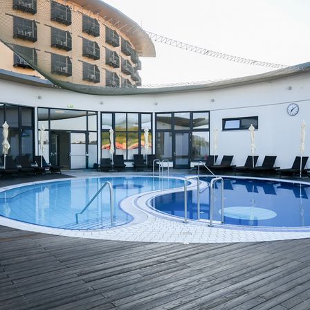 Ein Resort mit Schwimmbad, Liegestühlen und einem modernen Gebäude mit Balkonen und einer Uhr.