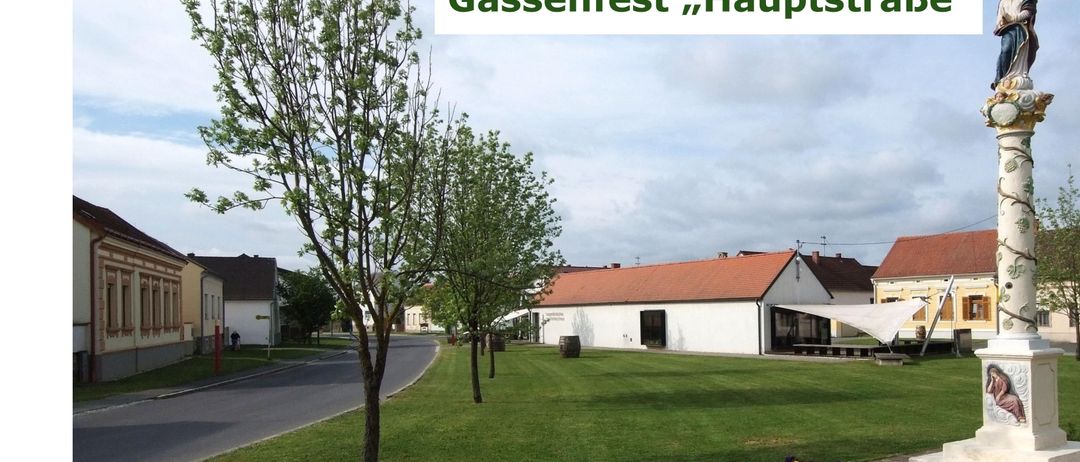 Ein Plakat, das das Gassenfest auf der Hauptstraße ankündigt, geplant für Freitag, 28. August 2026, ab 18:00 Uhr. Das Plakat zeigt ein grünes Feld, Bäume und Gebäude im Hintergrund.
