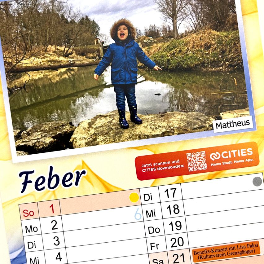 Ein lächelndes Kind steht auf einem Felsen am Teich und trägt eine blaue Jacke und Stiefel. Der Hintergrund zeigt eine verschwommene Landschaft mit Bäumen und einem Haus. Unter dem Bild befindet sich ein Kalender mit dem Monat Februar und einem QR-Code für eine Städte-App.