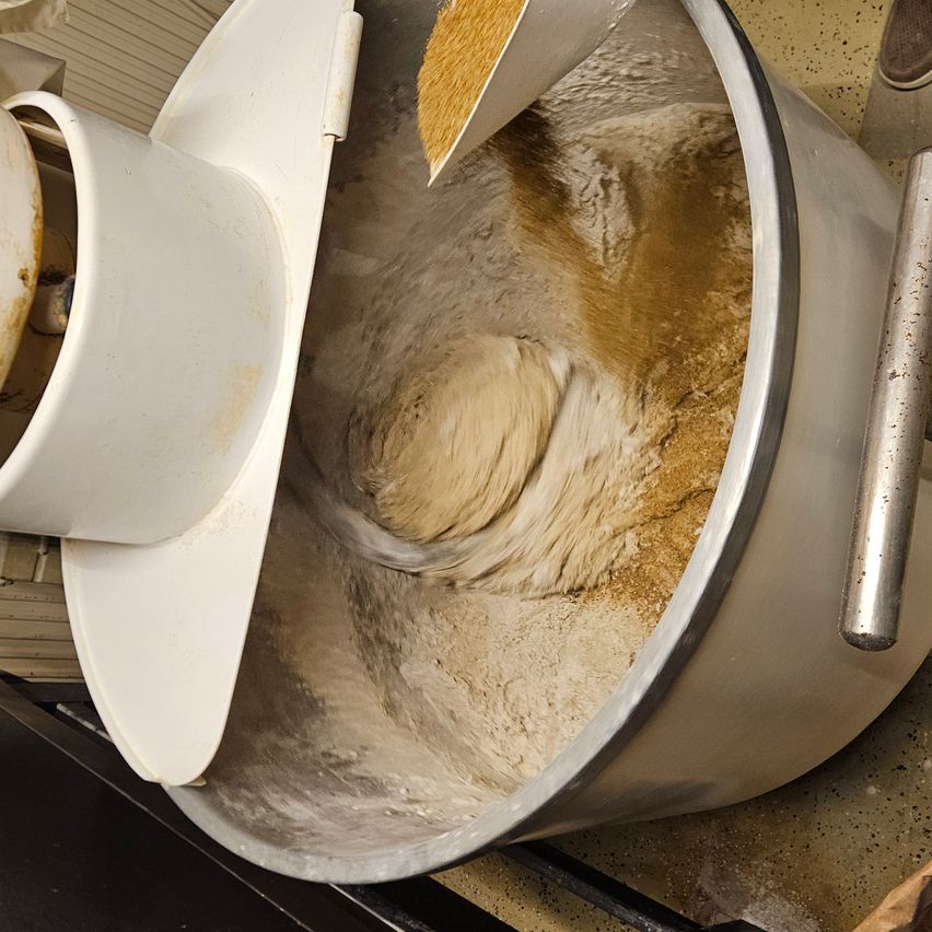 Eine Nahaufnahme eines Mixers mit Teig und Getreide, von oben gesehen. Der Teig wird gründlich gemischt.
