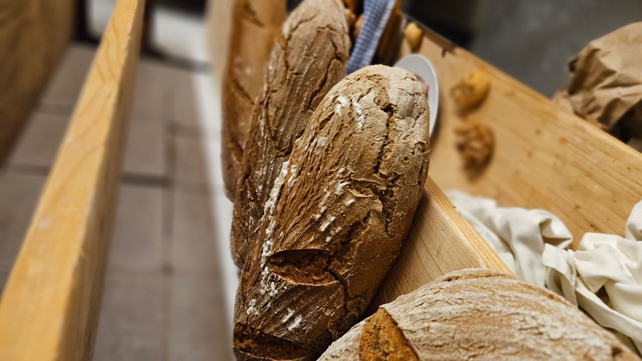 Eine Nahaufnahme mehrerer Laibe braunen Brotes mit strukturierter Kruste und Mehlbestäubung auf einem Holztisch.