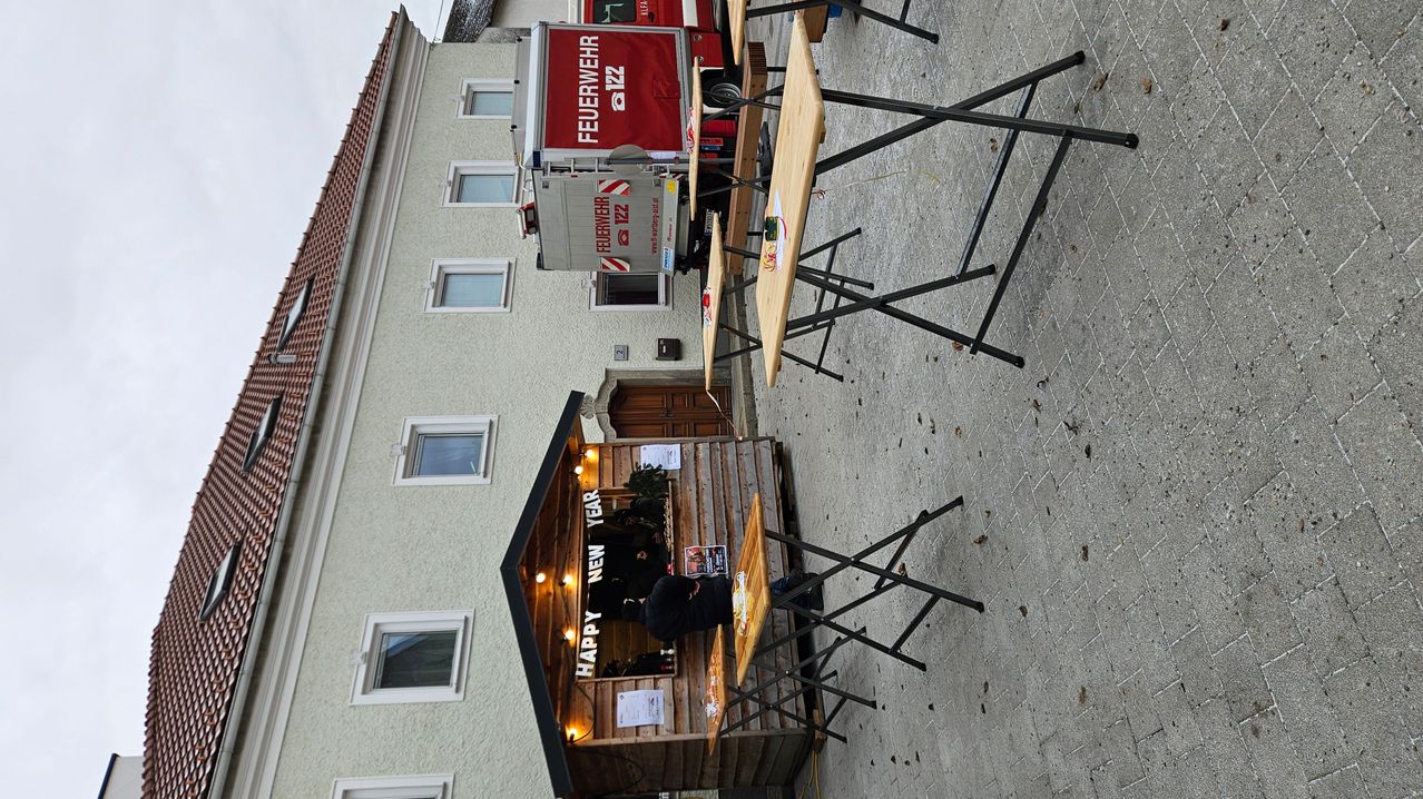 Eine Luftaufnahme eines Gebäudes mit mehreren Fenstern, einem Happy New Year-Schild, einem Feuerwehrauto und mehreren Tischen und Stühlen im Freien.