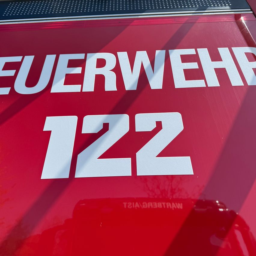 Ein roter Feuerwehrwagen mit den Worten 'Feuerwehr' und der Nummer '122' deutlich sichtbar. Der Hintergrund ist unscharf.