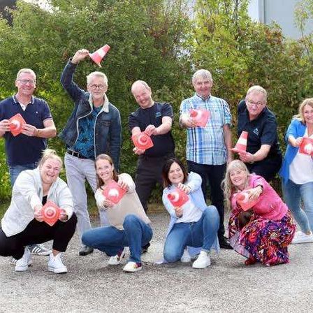 Eine Gruppe von Menschen, sowohl Männer als auch Frauen, posiert für ein Foto mit orangefarbenen Verkehrskegel. Sie alle lächeln und halten die Kegel auf verschiedene Weise.