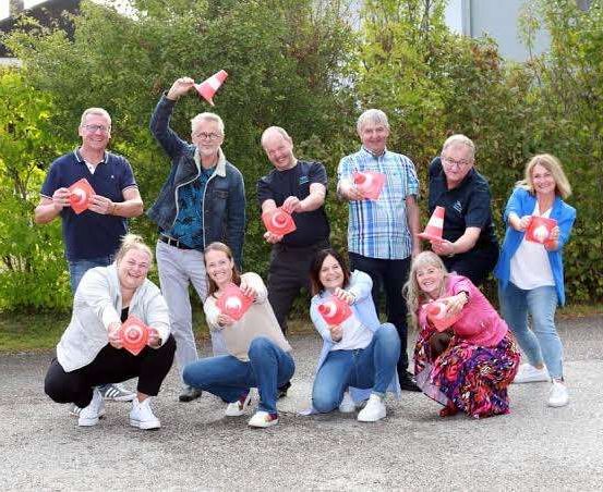 Eine Gruppe von Menschen, sowohl Männer als auch Frauen, posiert für ein Foto mit orangefarbenen Verkehrskegel. Sie alle lächeln und halten die Kegel auf verschiedene Weise.