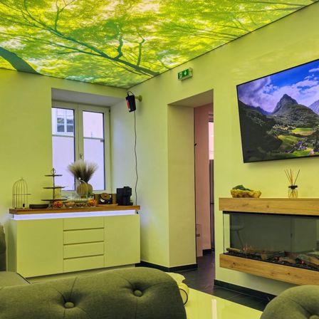 Ein gemütliches Zimmer mit einer grünen Baumdecke, einer gelben Wand und einem Tisch mit Essen. Es gibt einen modernen Kamin, einen Fernseher und ein Fenster mit Aussicht.