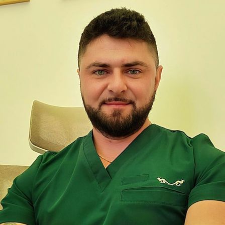 Ein Mann mit Bart und grünem Hemd mit Logo auf einem Stuhl in einem Raum sitzend.