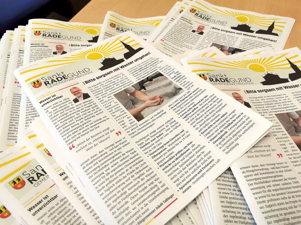 A stack of German newspapers, Sankt Radegund, feature an article with a picture of a person holding a faucet and text about water conservation.