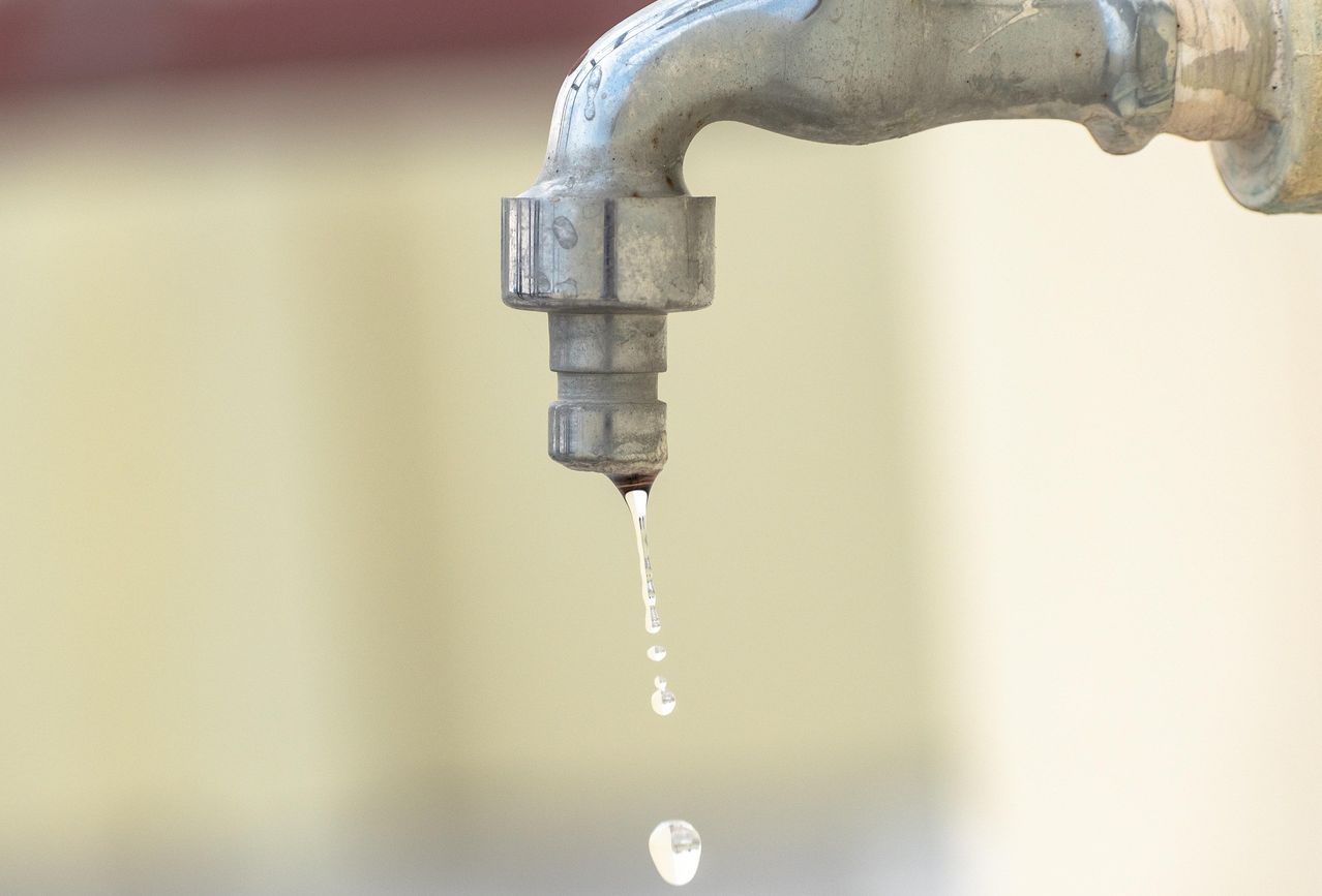 Nahaufnahme eines Wasserhahns, der tropft, mit Tropfen, die gegen einen hellen Hintergrund fallen.