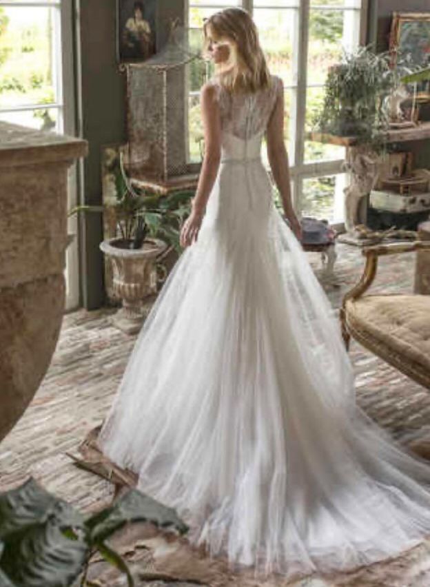 Eine Frau in einem Hochzeitskleid steht in einem Zimmer mit Pflanzen und Glasfenstern.