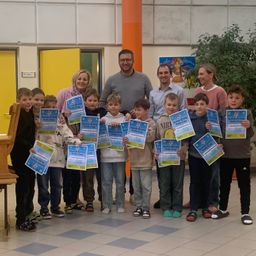 Eine Gruppe von Kindern in einem Schulflur, alle mit Urkunden in der Hand, posiert für ein Foto. Die Kinder stehen vor einem Mann und einer Frau mit lächelnden Gesichtern.