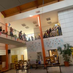 Eine Gruppe von Kindern steht auf dem Balkon eines Gebäudes, ein Kind hält einen Spielzeughund und ein anderes ein Banner.