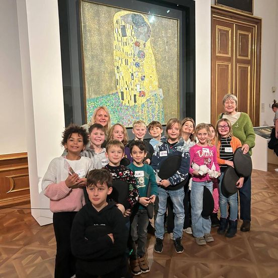 Eine Gruppe von Kindern und zwei Erwachsenen posiert für ein Foto in einem Museum vor einem Gemälde von Gustav Klimt.