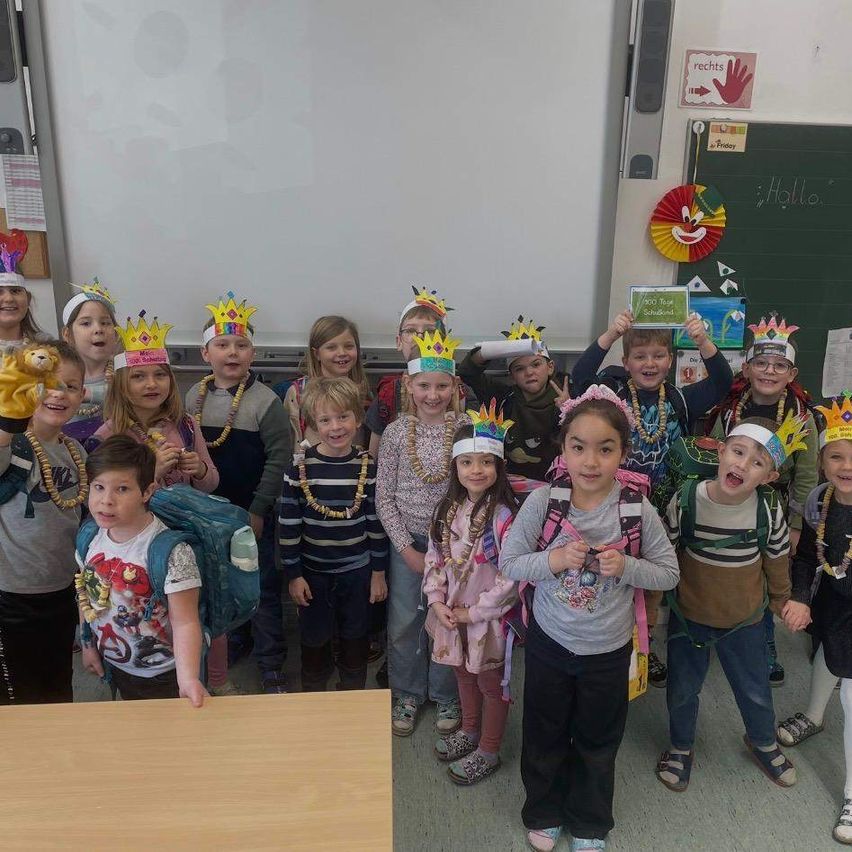 Eine Gruppe von Kindern im Klassenzimmer mit Kronen und Halsketten, die für ein Foto posieren, mit einer Tafel im Hintergrund.