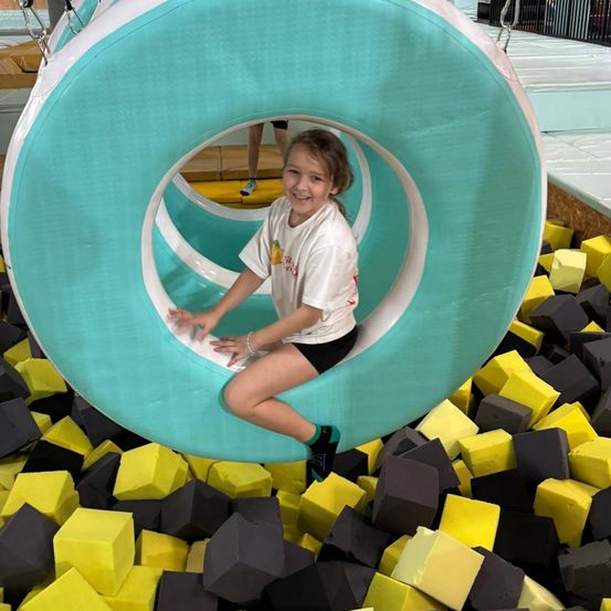 Ein kleines Mädchen ist in einem großen aufblasbaren Ring in einem Indoor-Trampolinpark und posiert lächelnd für ein Foto.
