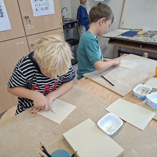Zwei Jungen arbeiten in einem Raum an einem Bastelprojekt. Sie haben Papiere und eine Schüssel mit Materialien auf dem Tisch. Ein Junge hält eine Schere.