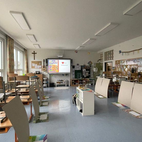 Ein leerer Klassenraum mit Schreibtischen und Stühlen, einer Projektionsleinwand an der Wand und Pinnwänden an den Wänden.
