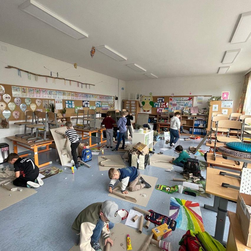 Mehrere Kinder sind in einem Klassenzimmer in ein Kunstprojekt vertieft, umgeben von verschiedenen Materialien und Kunstwerken an den Wänden.