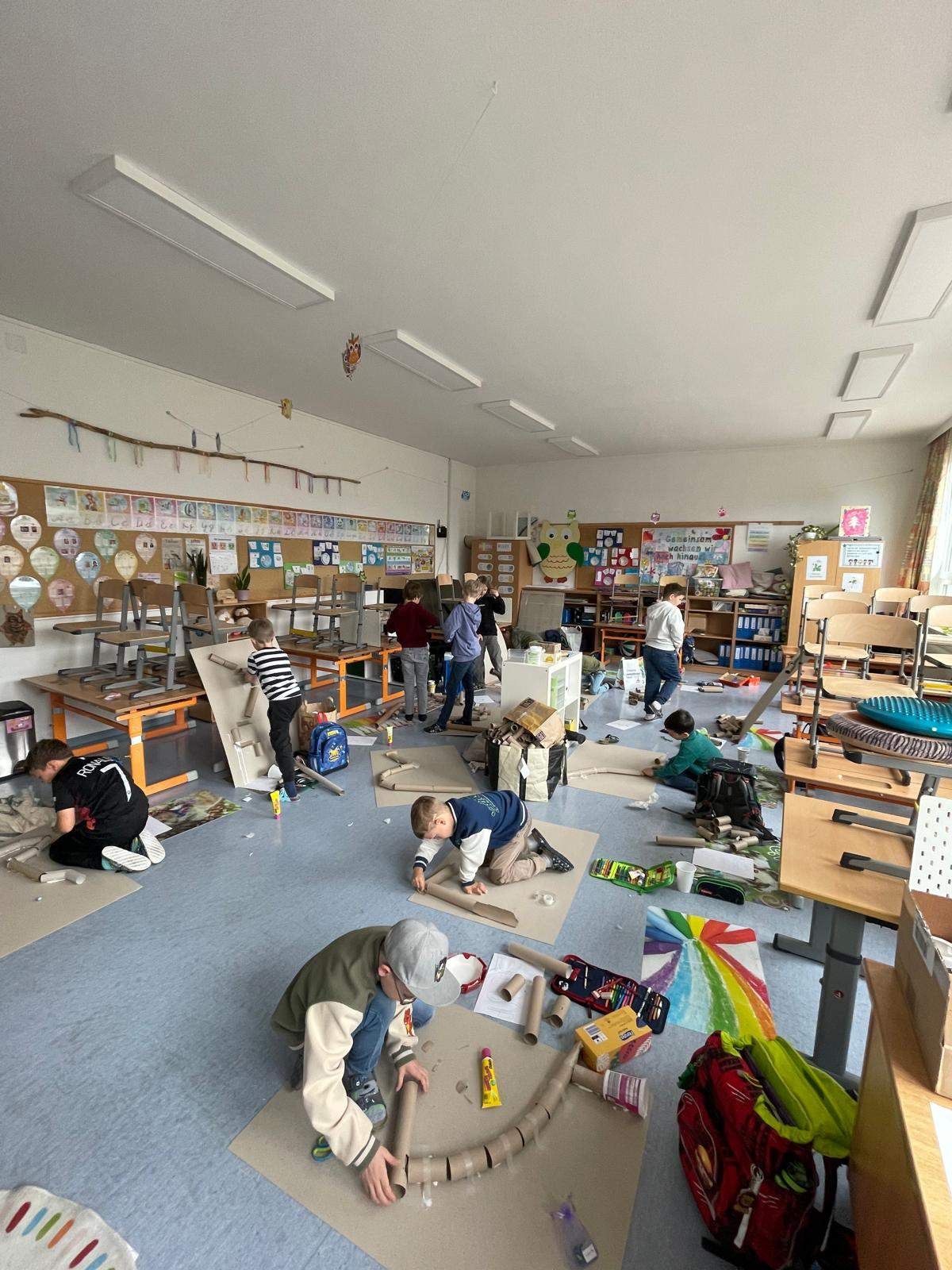 Mehrere Kinder sind in einem Klassenzimmer in ein Kunstprojekt vertieft, umgeben von verschiedenen Materialien und Kunstwerken an den Wänden.