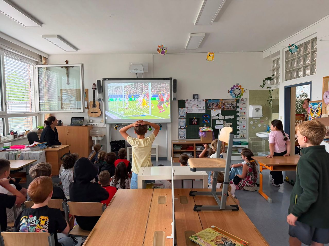 Ein Klassenzimmer mit Kindern, die ein Fußballspiel auf einer Projektionsleinwand sehen. Ein Junge bedeckt sein Gesicht mit den Händen.