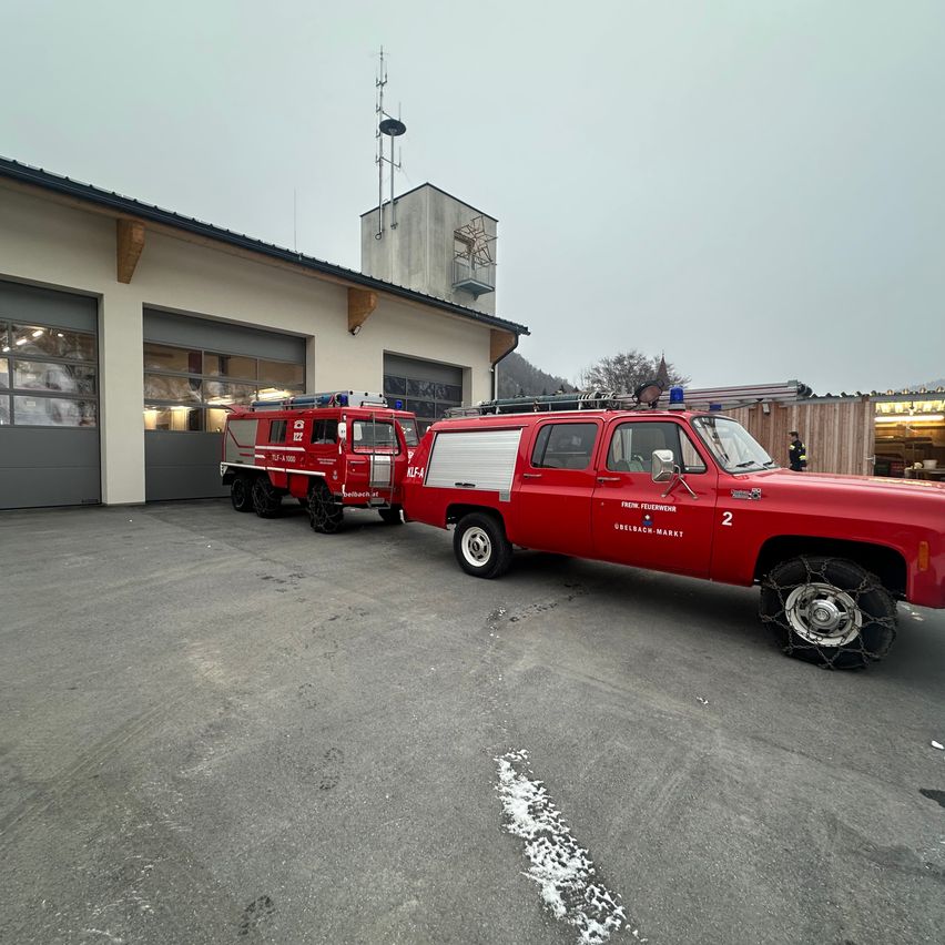 Zwei rote Rettungsfahrzeuge sind vor einem Gebäude mit zwei Garagen geparkt, und eine Person steht neben einer Holzwand.