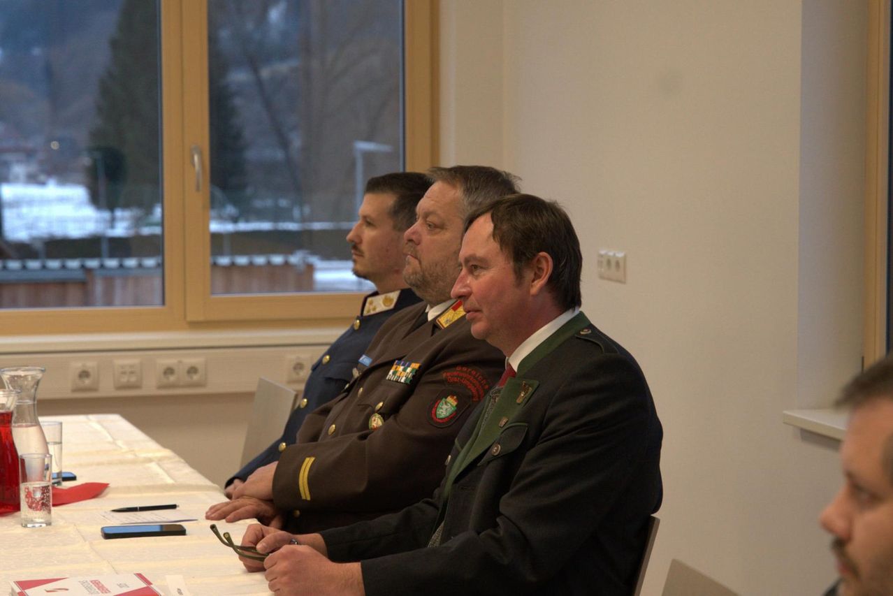 Drei Männer in Militäruniformen sitzen in einem Konferenzraum an einem Tisch. Sie schauen zur Kamera. Hinter ihnen ist ein Fenster mit Blick nach draußen zu sehen.