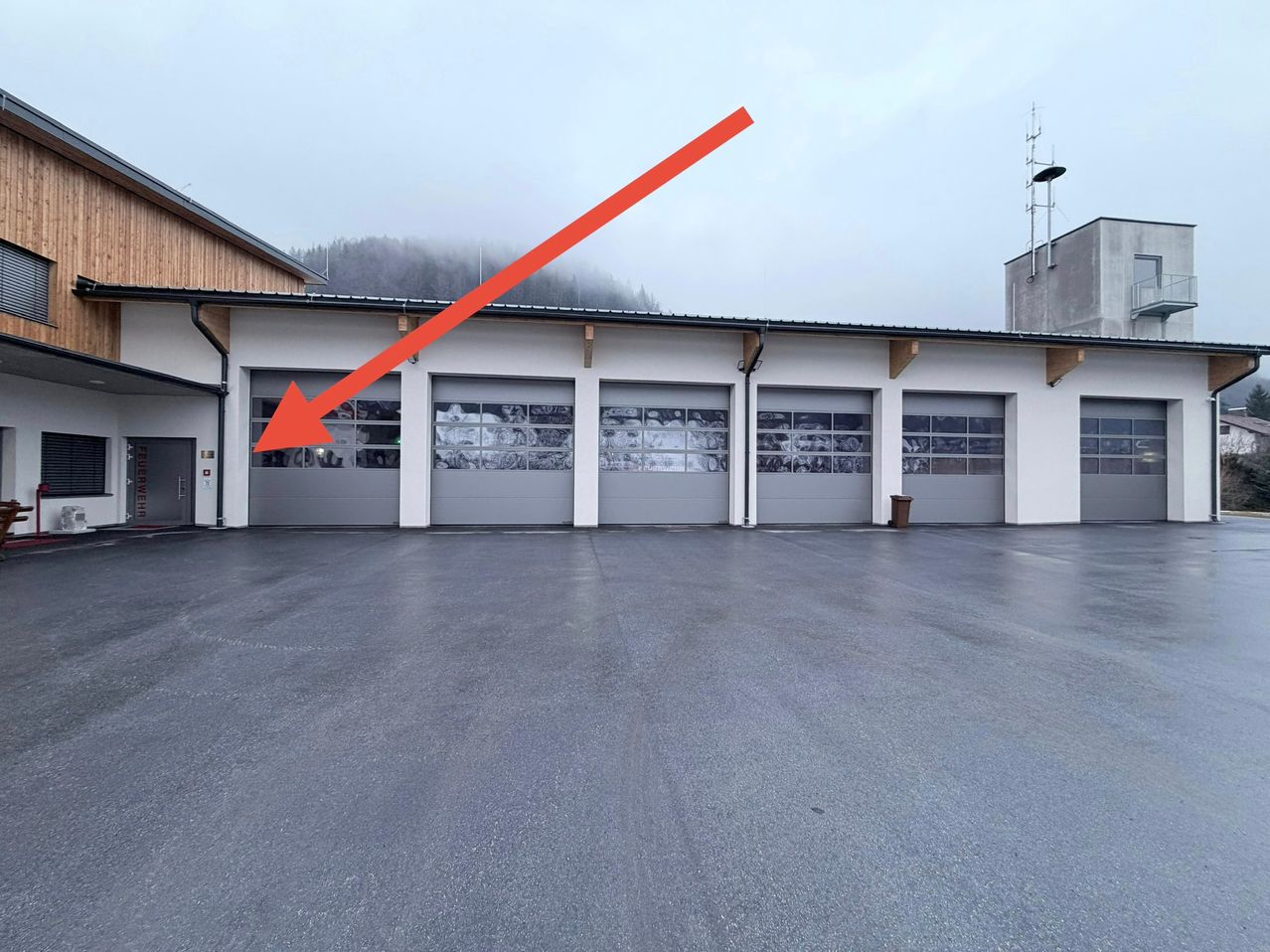 Ein Gebäude mit vier großen Garagentoren, jedes mit einem einzigartigen Bild. Ein orangefarbener Pfeil zeigt auf die Spitze des Gebäudes.