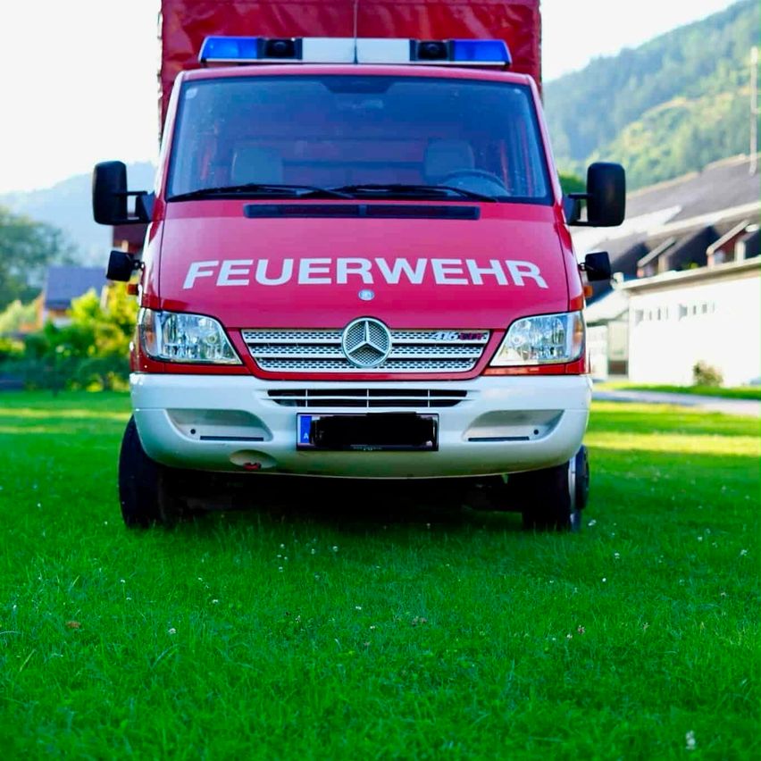 A red fire truck with the word 'Feuerwehr' on the front is parked on a green lawn.
