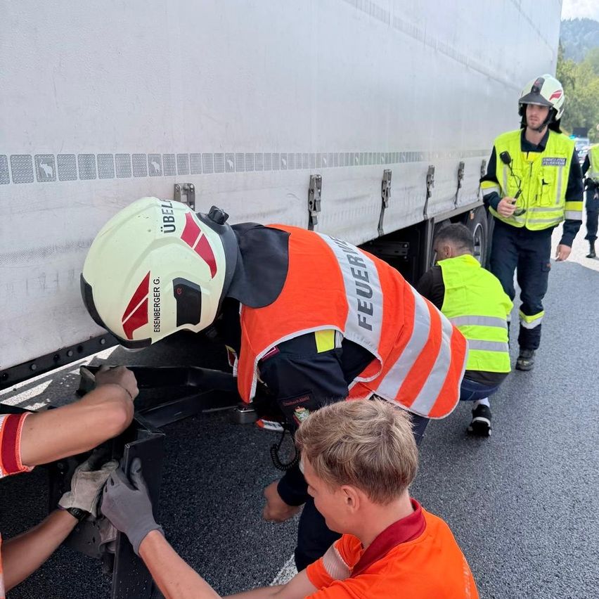 Eine Gruppe von Feuerwehrleuten in orangefarbenen Uniformen arbeitet an der Seite eines Lastwagens. Einer trägt einen Helm und Handschuhe, während ein anderer in der Nähe steht.