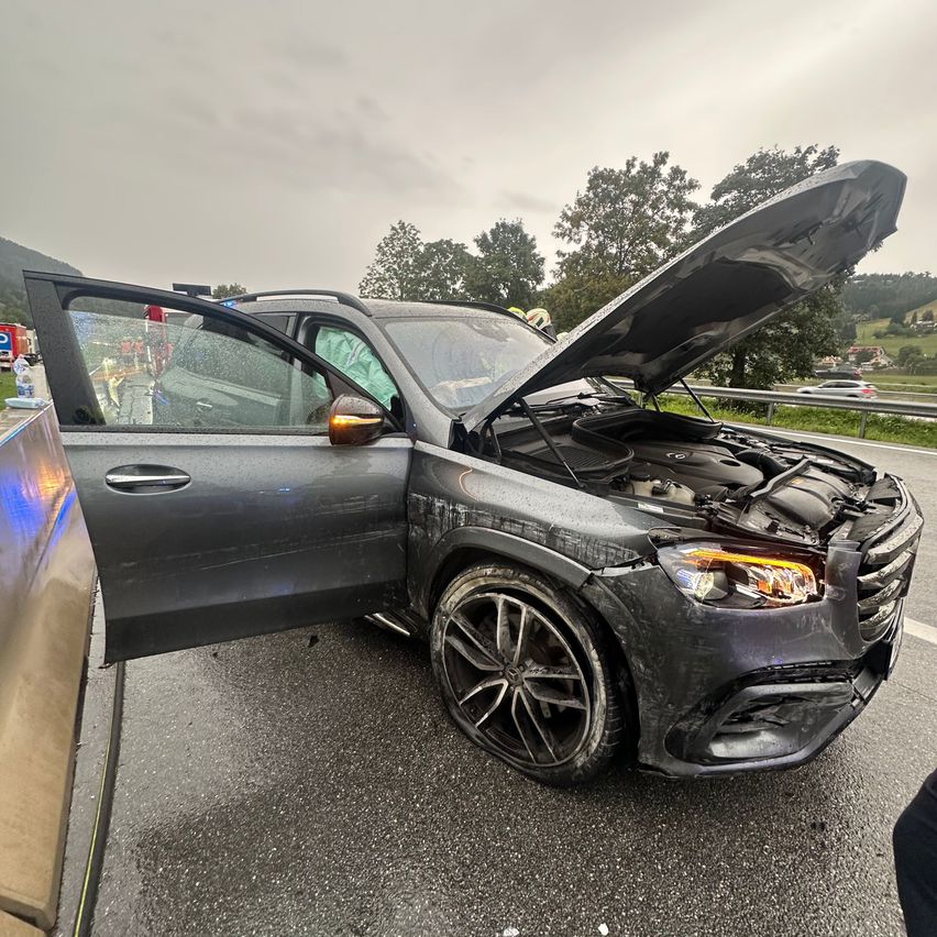 Ein beschädigter schwarzer SUV mit offenem Motorhaube am Straßenrand, möglicherweise nach einem Unfall.