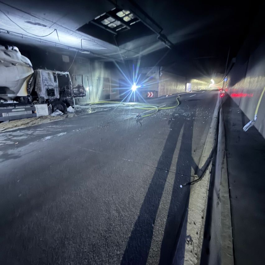 An inside view of a tunnel with a damaged vehicle and bright lights. The road is empty, and a shadow is cast on the ground.