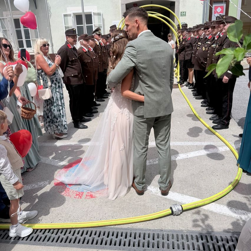 A wedding ceremony is taking place with a groom and bride standing near a yellow hose, surrounded by people in uniform.
