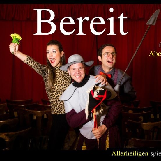 Drei Menschen in Kostümen stehen vor einem roten Vorhang mit den Worten 'BEREIT FURS ABENTEUER' darüber. Die Frau hält eine Blume.