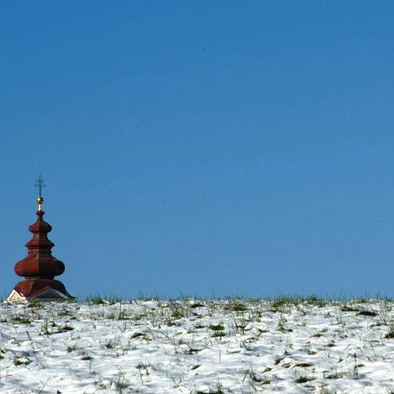 Ein roter Turm steht auf einem verschneiten Hügel unter einem klaren blauen Himmel.