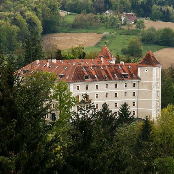 Ein großes weißes Gebäude mit einem roten Dach, eingebettet zwischen Bäumen und mit Blick auf ein Feld.