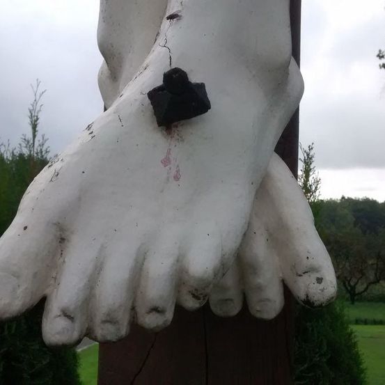 Ein Nahaufnahme eines weißen Statuenfußes zeigt einen großen schwarzen Stein in der Mitte. Die Statue ist auf einem braunen Pfosten montiert mit einem bewölkten Himmel im Hintergrund.