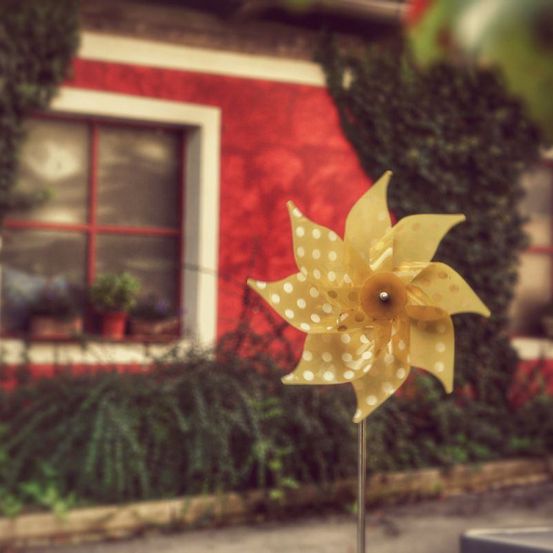 Ein verschwommenes Bild eines gelben Windrads mit weißen Punkten vor einem roten Haus mit Fenster und Topfpflanzen.