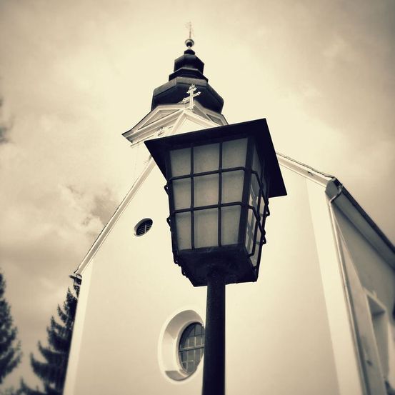 Ein schwarz-weißes Bild einer Kirche mit einem Turm und einem Kreuz. Ein Laternenpfahl steht vor der Kirche.