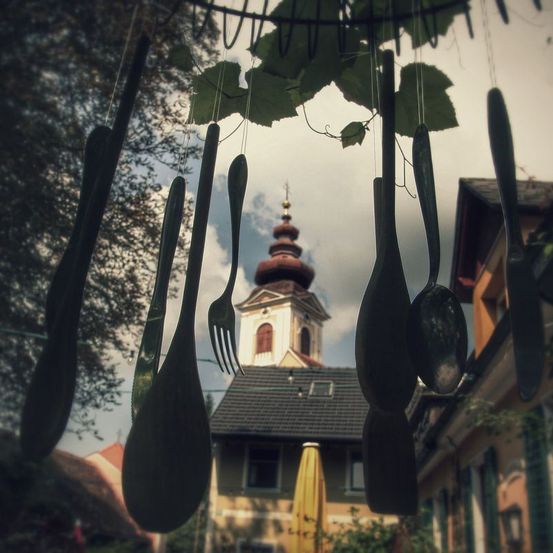Eine Sammlung von Löffeln und Gabeln hängt von den Ästen eines Baumes vor einer Kirche mit einem Kirchturm.