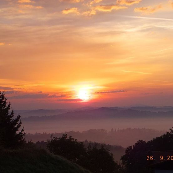 Sonnenaufgang an einem nebligen Morgen, mit der Sonne hinter Wolken. Mit Bergen bedeckt im Nebel und Bäumen unten. Datum: 26.9.20.