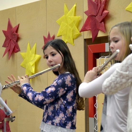 Vier junge Mädchen spielen Flöten in einem Klassenzimmer mit Sternendekorationen an der Wand.