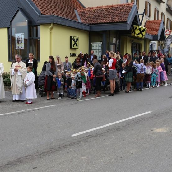 Eine religiöse Prozession findet auf der Straße statt, mit Menschen, die vor einem Gebäude mit dem Schriftzug 'BANK' stehen.