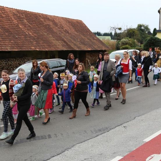 Eine große Gruppe von Erwachsenen und Kindern marschiert in einem Zug die Straße entlang, mit mehreren geparkten Autos in der Nähe.