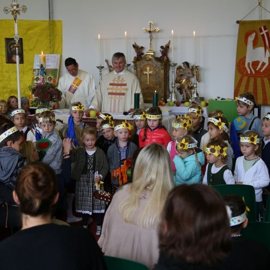 Eine religiöse Zeremonie mit Kindern, die Stirnbänder tragen, findet in einer Kirche mit zwei Priestern statt. Kerzen und Blumen sind auf dem Altar.