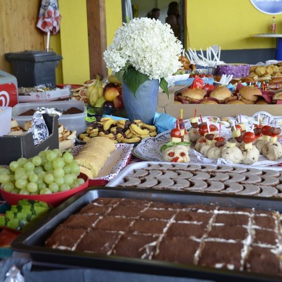 Ein Buffettisch voller verschiedener Speisen, einschließlich Sandwiches, Obst und Desserts, zusammen mit einer weißen Blumenarrangement.