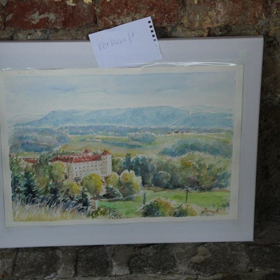 Ein Aquarellbild in einem weißen Rahmen zeigt eine malerische Landschaft mit einem Schloss und Bergen in der Ferne.