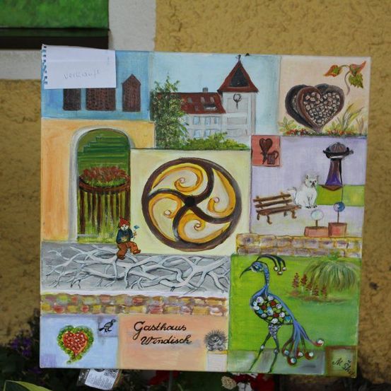 Ein Collage-Gemälde an einer gelben Wand mit verschiedenen Objekten, einer Person, einer Spirale, einer Katze, einem Haus und einem Vogel. Das Gemälde hat einen Zettel mit dem Wort 'Verkauft'.