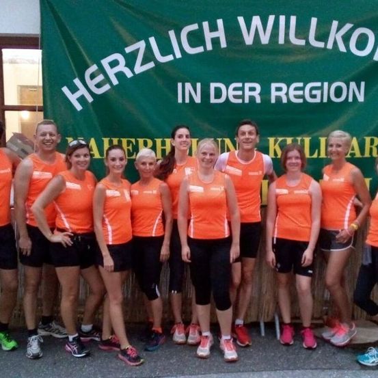 Eine Gruppe von Menschen in orangefarbener und schwarzer Sportbekleidung posiert für ein Foto vor einem grünen Banner.