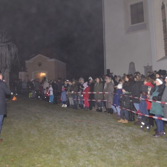 Eine Menschenmenge steht im Dunkeln vor einer Kirche. Sie sind durch Absperrungen getrennt. Ein Mann steht im Vordergrund mit einer brennenden Fackel.